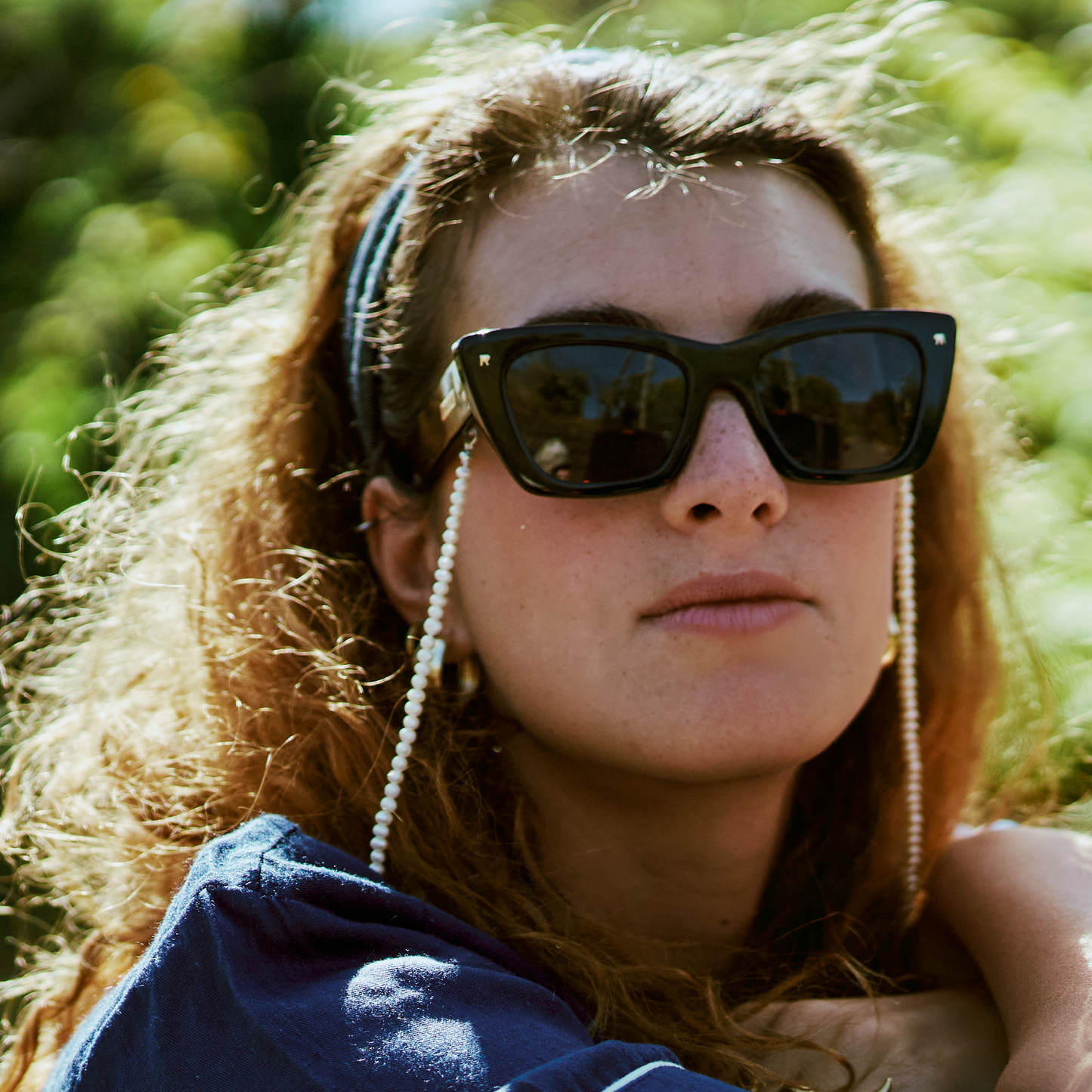 Woman wearing sunglasses with chain, blue headband, and blue top outdoors.